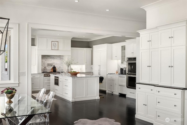 kitchen with a center island, stainless steel double oven, white cabinets, ornamental molding, and backsplash