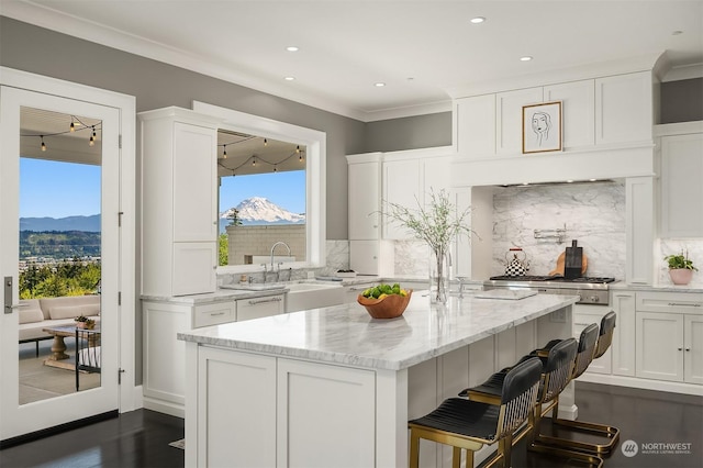 kitchen featuring decorative backsplash, a mountain view, white cabinets, a breakfast bar, and light stone counters