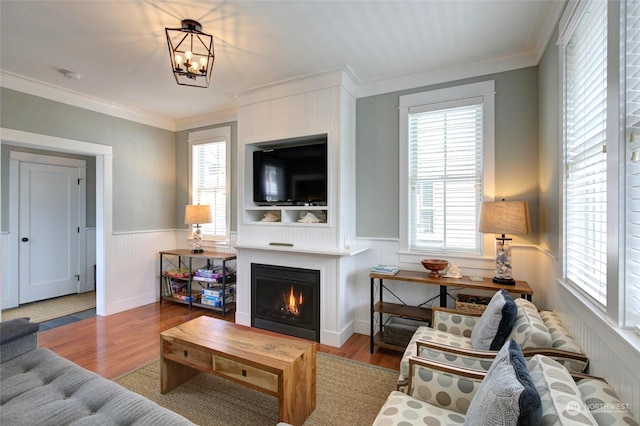 living area with a wainscoted wall, a lit fireplace, ornamental molding, and wood finished floors