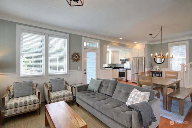 living room with a wainscoted wall, plenty of natural light, a chandelier, and ornamental molding