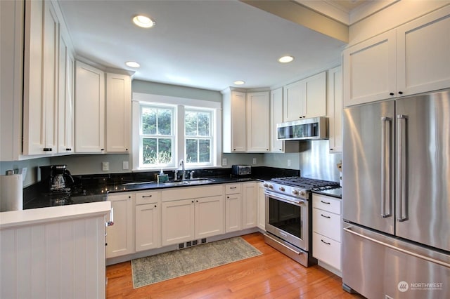 kitchen featuring light wood finished floors, premium appliances, dark countertops, a sink, and recessed lighting