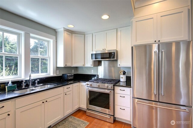 kitchen featuring high end appliances, recessed lighting, light wood-style floors, white cabinets, and a sink