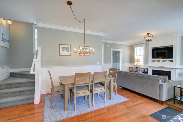 dining room featuring a lit fireplace, stairway, wainscoting, and light wood-type flooring