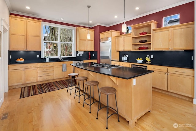 kitchen featuring a center island, light brown cabinetry, a kitchen bar, decorative light fixtures, and stainless steel appliances