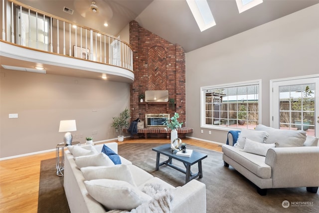 living room featuring hardwood / wood-style flooring, a brick fireplace, high vaulted ceiling, and a skylight