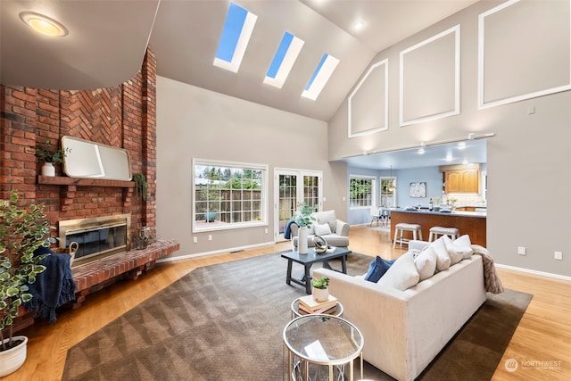 living room featuring a skylight, a fireplace, light hardwood / wood-style floors, and high vaulted ceiling