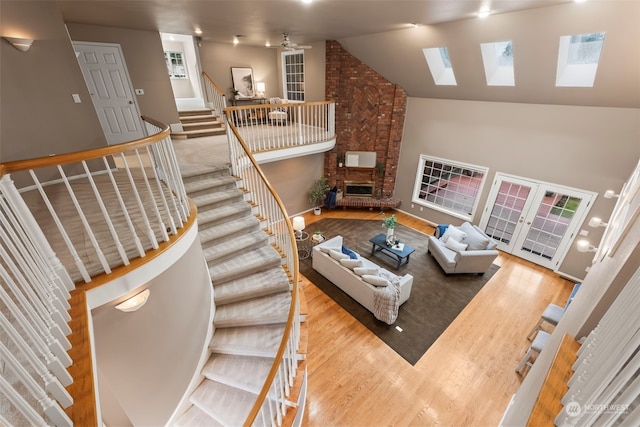 living room featuring ceiling fan, a skylight, high vaulted ceiling, a brick fireplace, and light wood-type flooring