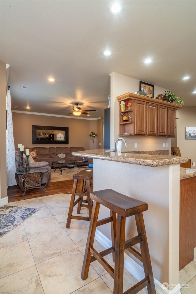 kitchen with light stone counters, ceiling fan, a breakfast bar, and kitchen peninsula