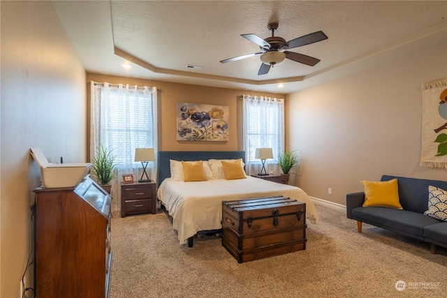 bedroom featuring a raised ceiling, light colored carpet, and ceiling fan