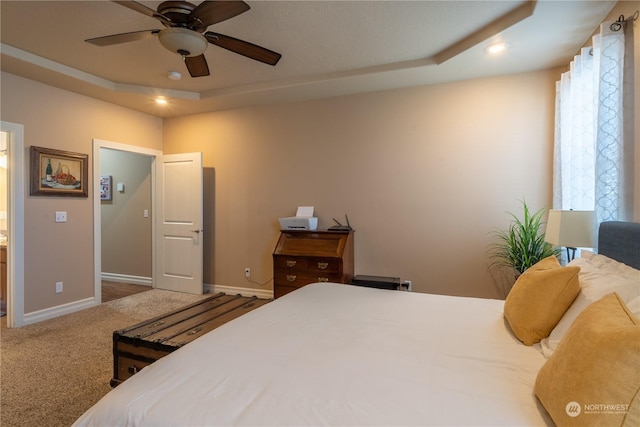 carpeted bedroom with ceiling fan and a tray ceiling