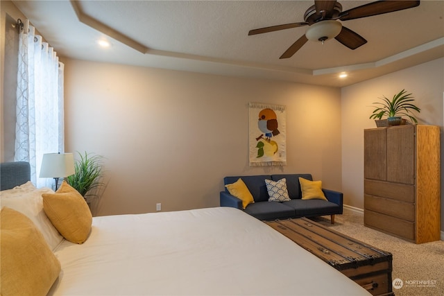 carpeted bedroom with a raised ceiling, ceiling fan, and multiple windows