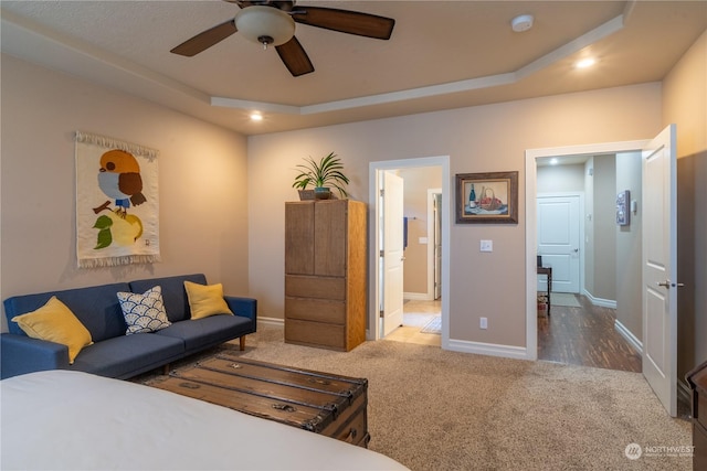 carpeted bedroom featuring a raised ceiling, ensuite bathroom, and ceiling fan