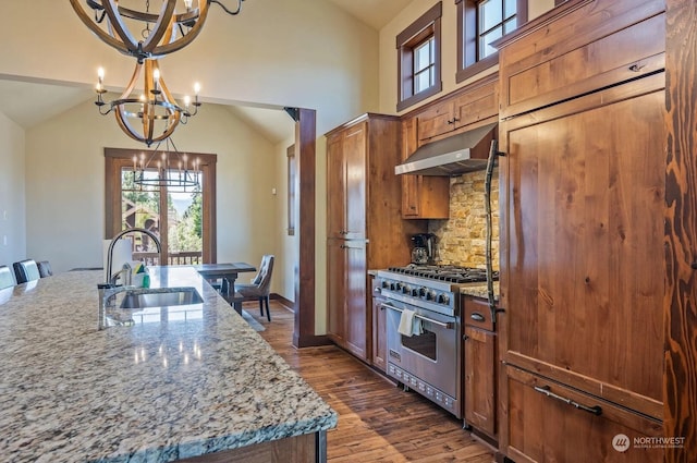 kitchen with designer stove, decorative backsplash, light stone countertops, an island with sink, and range hood