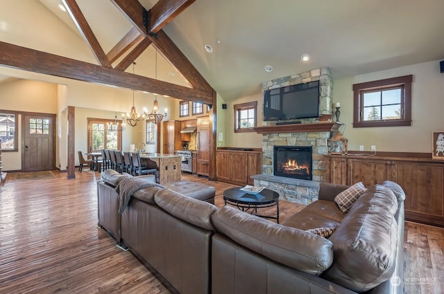 living room featuring a notable chandelier, beamed ceiling, a stone fireplace, wood-type flooring, and high vaulted ceiling