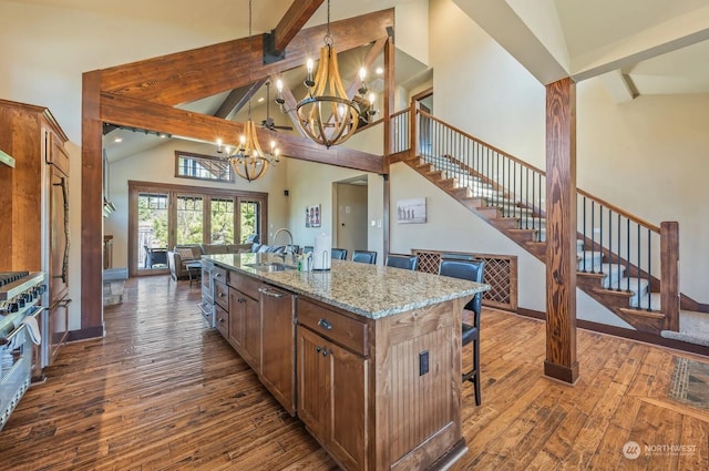 kitchen featuring pendant lighting, sink, light stone counters, an island with sink, and an inviting chandelier
