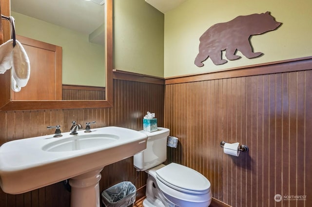 bathroom featuring sink, toilet, and wooden walls