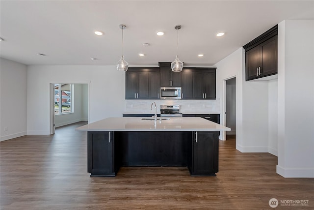 kitchen featuring light countertops, backsplash, appliances with stainless steel finishes, a sink, and an island with sink