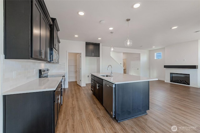 kitchen with light wood-style flooring, a sink, appliances with stainless steel finishes, tasteful backsplash, and a glass covered fireplace