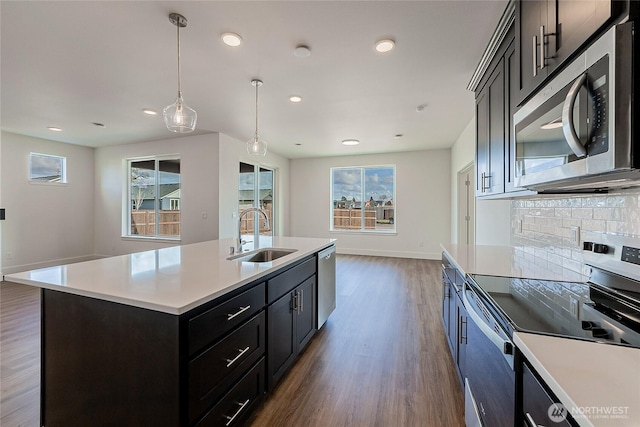 kitchen with a sink, light countertops, appliances with stainless steel finishes, dark wood-style floors, and tasteful backsplash