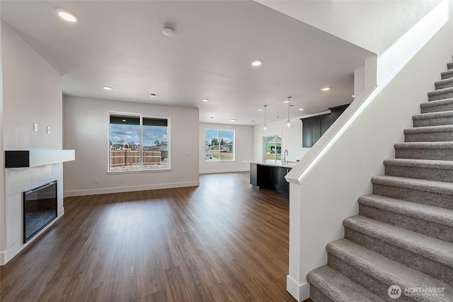 unfurnished living room with baseboards, dark wood finished floors, a tile fireplace, stairway, and recessed lighting