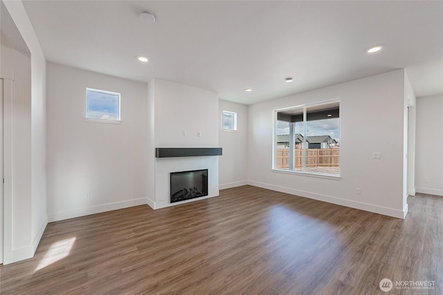 unfurnished living room featuring baseboards, a glass covered fireplace, wood finished floors, and recessed lighting