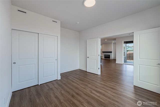 unfurnished bedroom with baseboards, visible vents, wood finished floors, a fireplace, and a closet