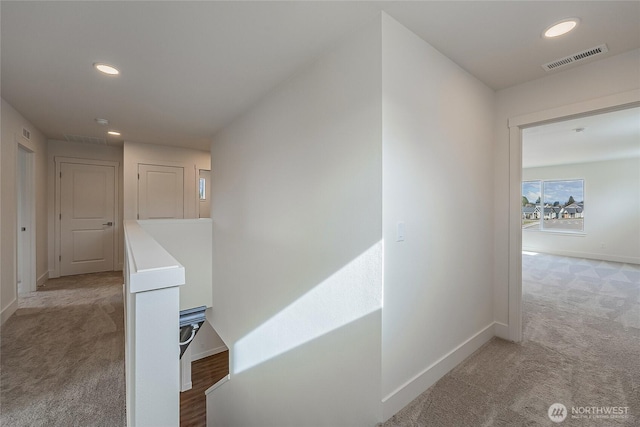 corridor with baseboards, visible vents, light colored carpet, and an upstairs landing