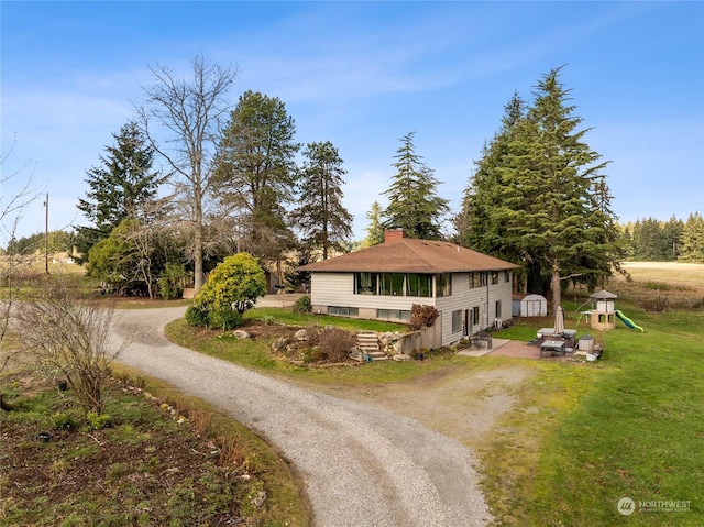 view of front of property with dirt driveway, a chimney, a front yard, and a playground