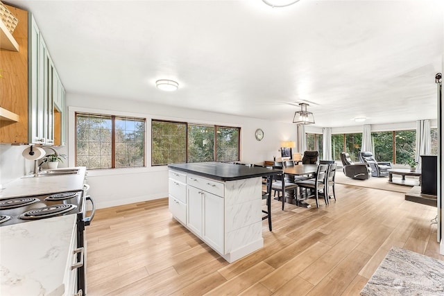 kitchen featuring light wood finished floors, open floor plan, a kitchen bar, white cabinetry, and a sink