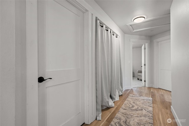 corridor with light wood-style floors, attic access, and baseboards