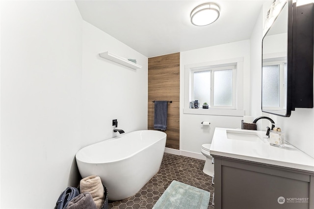 bathroom featuring toilet, wood walls, vanity, baseboards, and a soaking tub