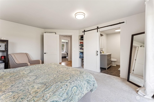 carpeted bedroom featuring a barn door, connected bathroom, baseboards, and a sink