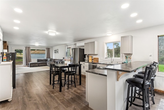 kitchen featuring a peninsula, a breakfast bar, a sink, appliances with stainless steel finishes, and dark countertops