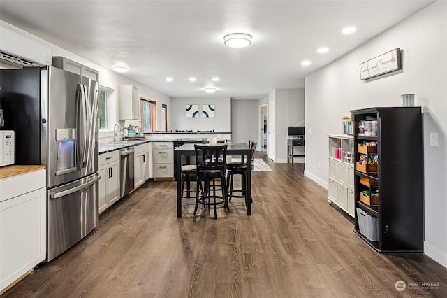 kitchen featuring stainless steel appliances, a peninsula, dark wood-style flooring, baseboards, and a kitchen bar