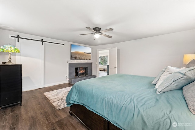 bedroom with a brick fireplace, a barn door, a ceiling fan, and wood finished floors