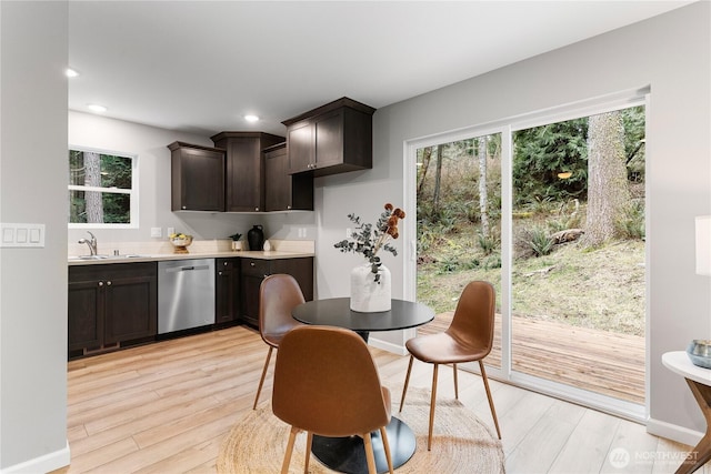 kitchen with dark brown cabinetry, light wood-style flooring, dishwasher, and a sink