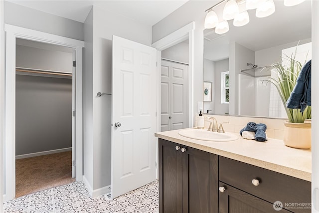 bathroom featuring vanity, baseboards, walk in shower, a walk in closet, and backsplash