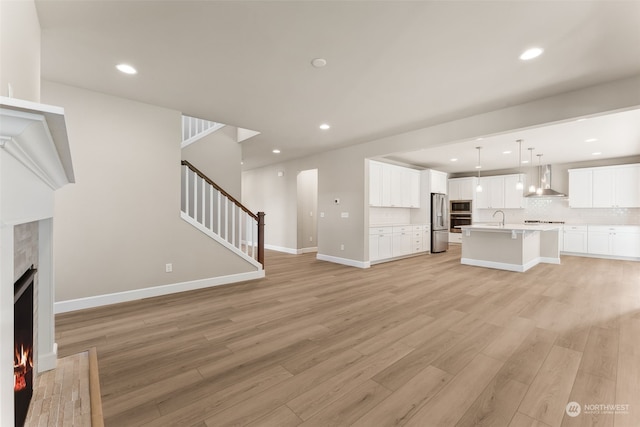 unfurnished living room with sink, a high end fireplace, and light hardwood / wood-style flooring