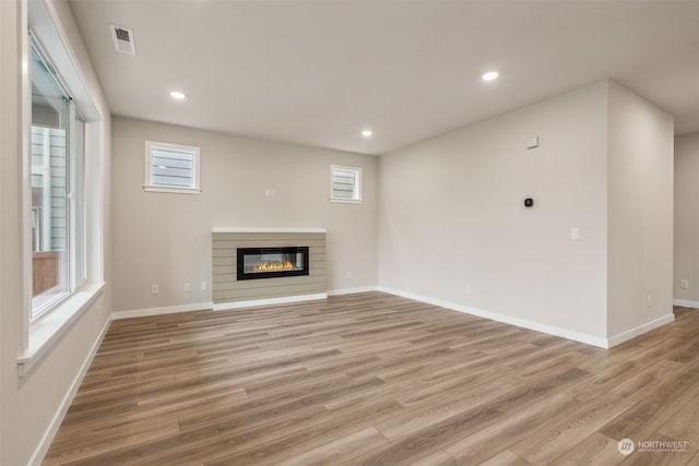 unfurnished living room with visible vents, light wood finished floors, recessed lighting, a glass covered fireplace, and a wealth of natural light