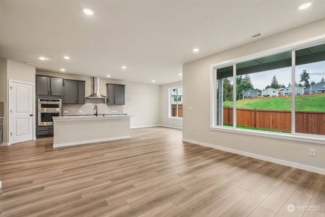 kitchen featuring visible vents, stainless steel double oven, a sink, wall chimney exhaust hood, and tasteful backsplash