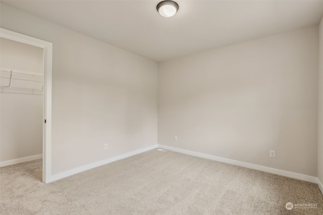 unfurnished bedroom with a spacious closet, baseboards, a closet, and light carpet