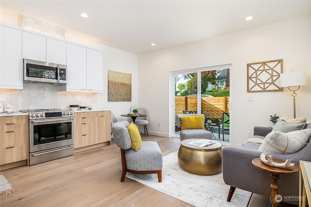 interior space featuring appliances with stainless steel finishes, white cabinetry, light brown cabinetry, backsplash, and light hardwood / wood-style flooring