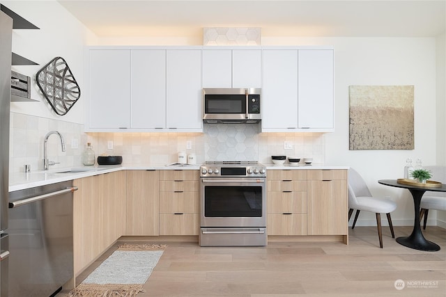 kitchen featuring light hardwood / wood-style floors, white cabinets, backsplash, and appliances with stainless steel finishes