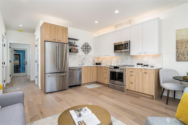 kitchen featuring decorative backsplash, white cabinets, light wood-type flooring, sink, and stainless steel appliances