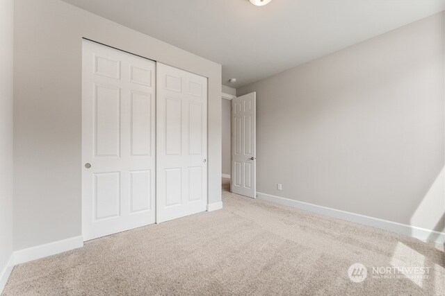 unfurnished bedroom with light colored carpet and a closet