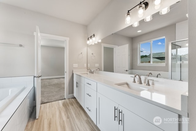 bathroom featuring wood-type flooring, tiled bath, and vanity