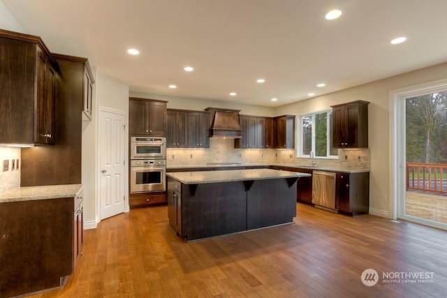 kitchen with a center island, custom exhaust hood, appliances with stainless steel finishes, hardwood / wood-style flooring, and sink