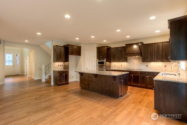 kitchen with a center island, custom exhaust hood, light hardwood / wood-style floors, sink, and light stone counters