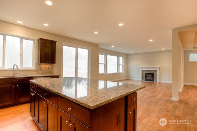 kitchen with sink, backsplash, light stone countertops, a kitchen island, and light hardwood / wood-style floors