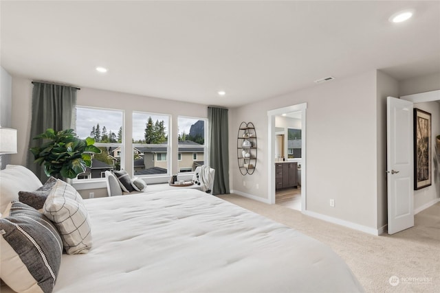 bedroom with ensuite bathroom and light carpet